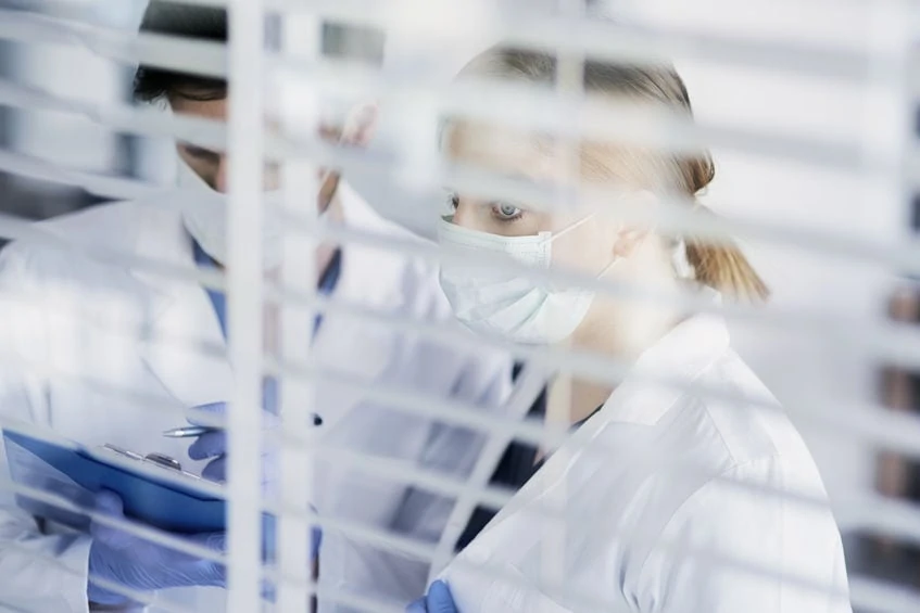 Pair of doctors behind the blinds of patient room